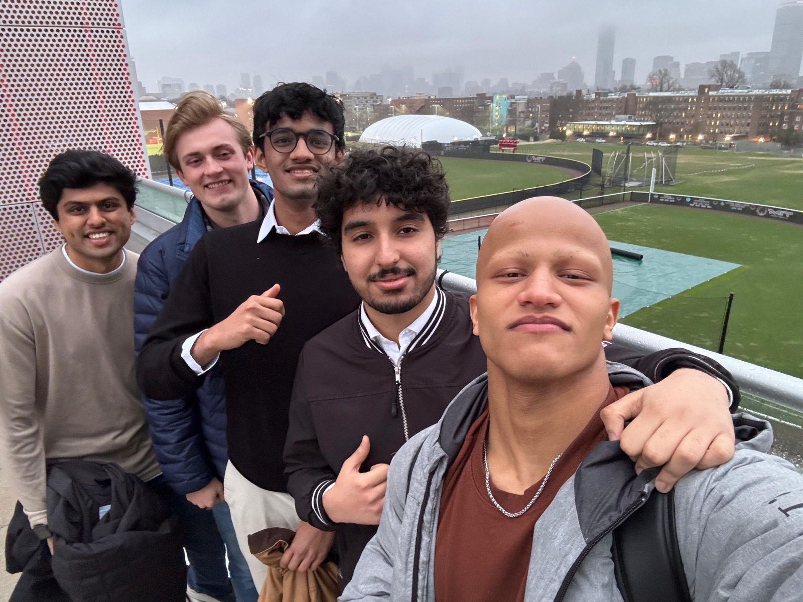 Five friends on an MIT rooftop with the Boston skyline in fog